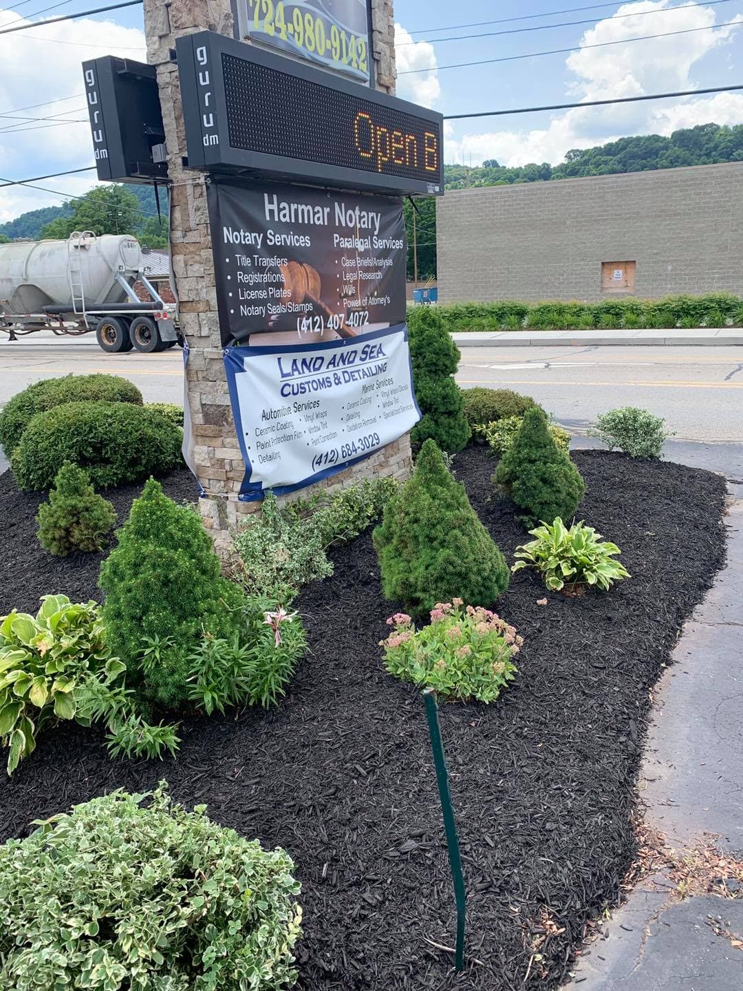 Signage for Harmar Notary and Land and Sea, with landscaped bushes and mulch in foreground.