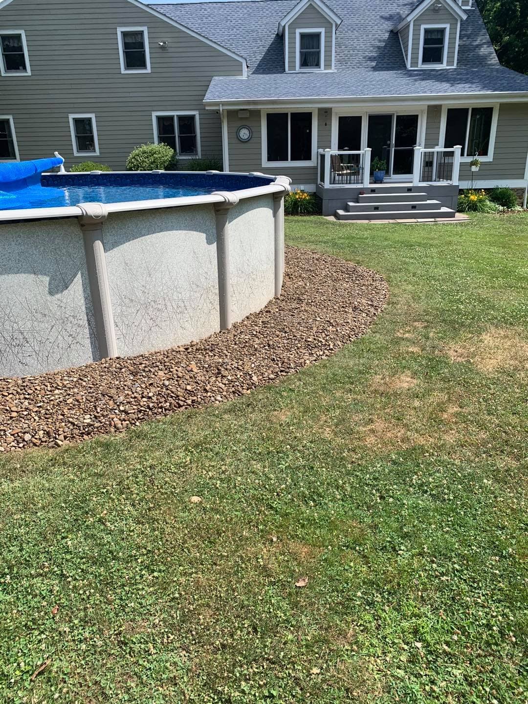 Above-ground pool with stone landscaping in a backyard of a house with patio and garden.