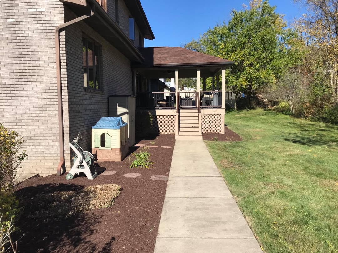 Backyard view of a home with a porch, walkway, and landscaped garden area.
