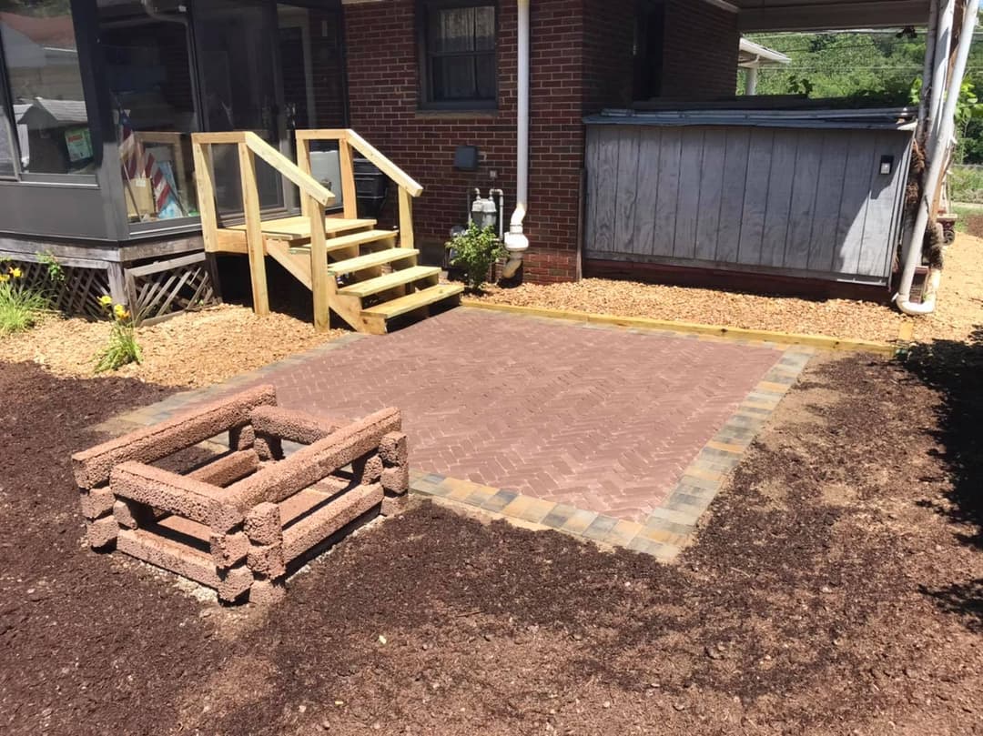 Patio area with herringbone brick pattern, wooden steps, and landscaping details.