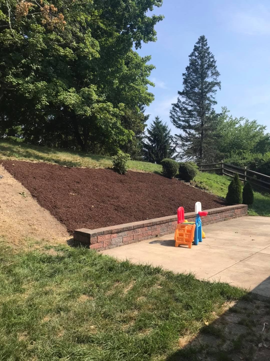 Play area with colorful toys beside a landscaped yard featuring freshly mulched plants.