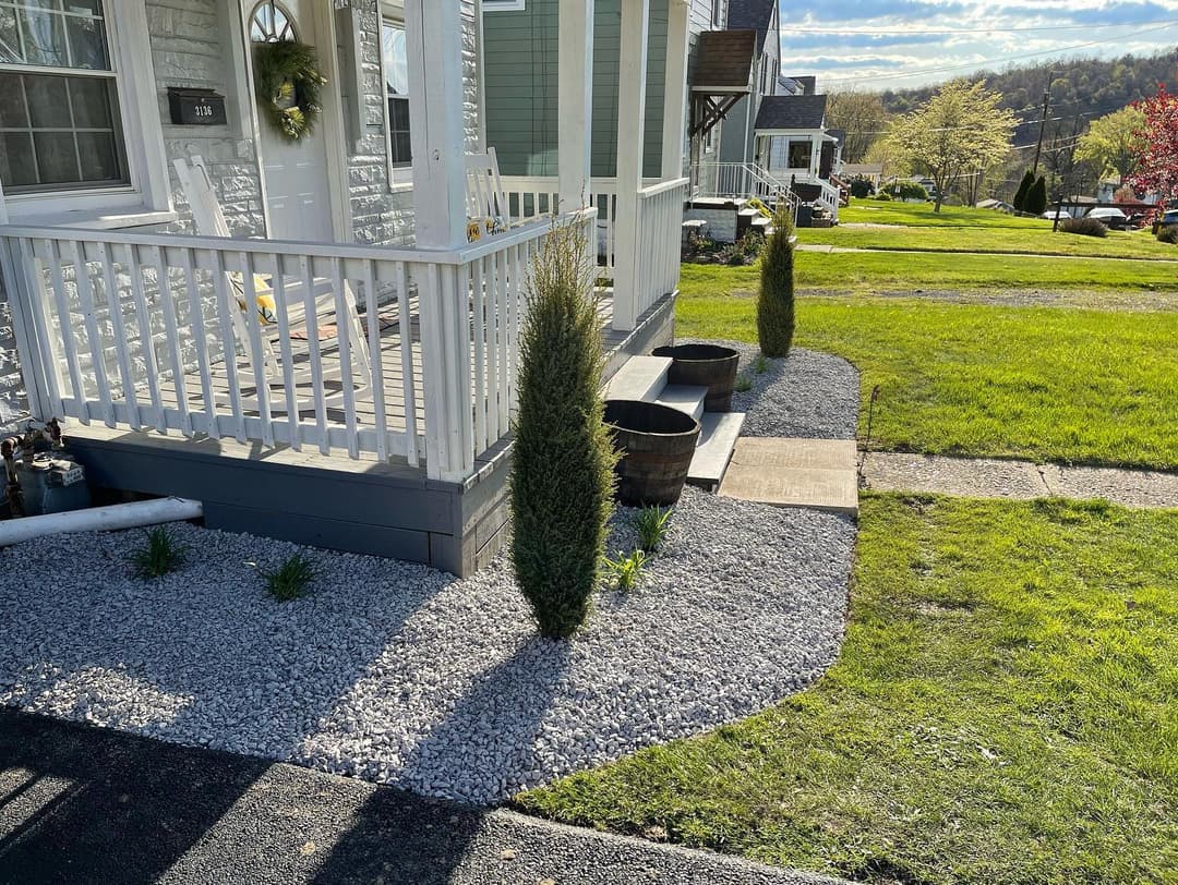 Front porch with greenery and decorative stones, showcasing a well-maintained yard.