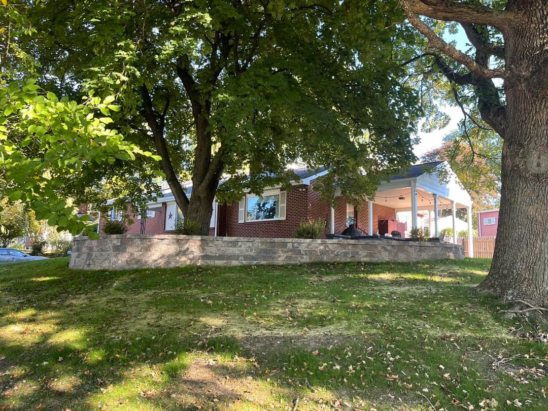 Brick house with porch, surrounded by trees and grass on a sunny day.