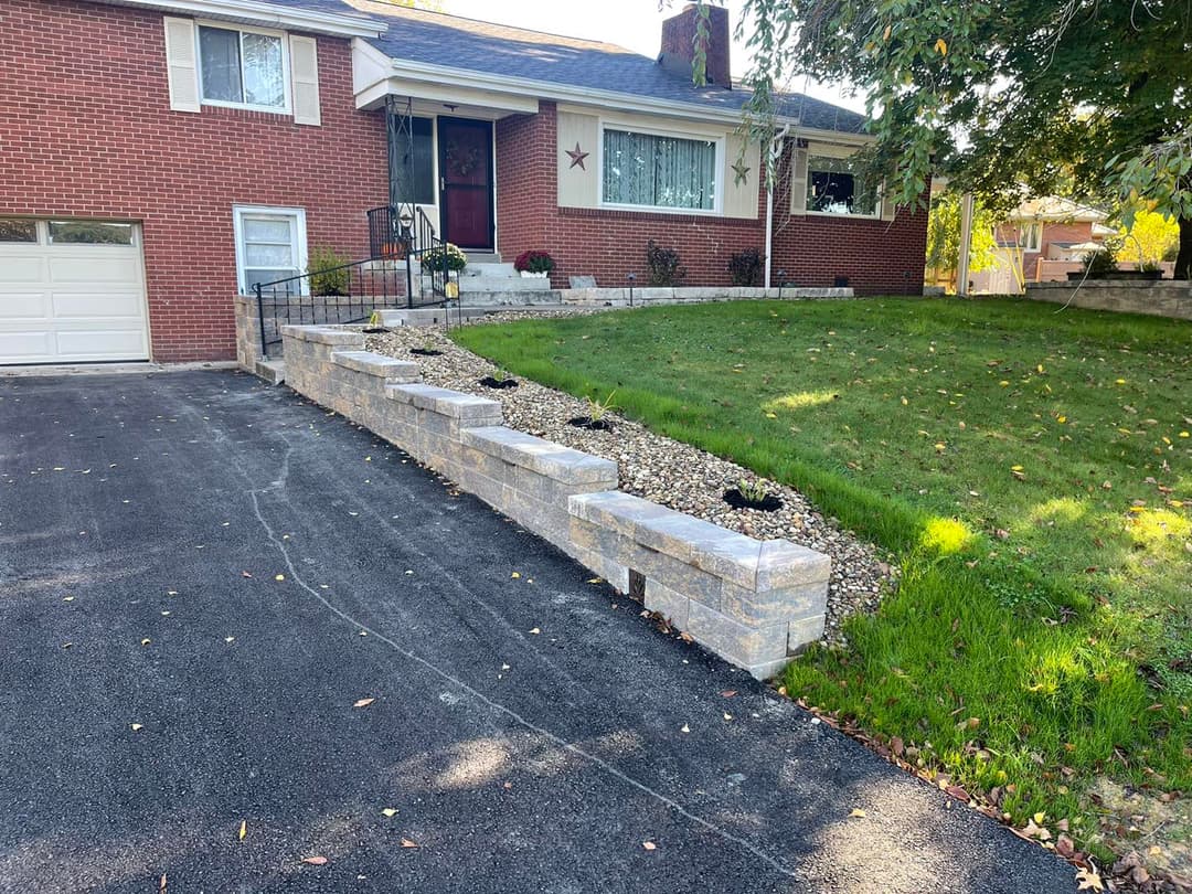 Front yard with landscaped stone retaining wall and driveway leading to red brick house.