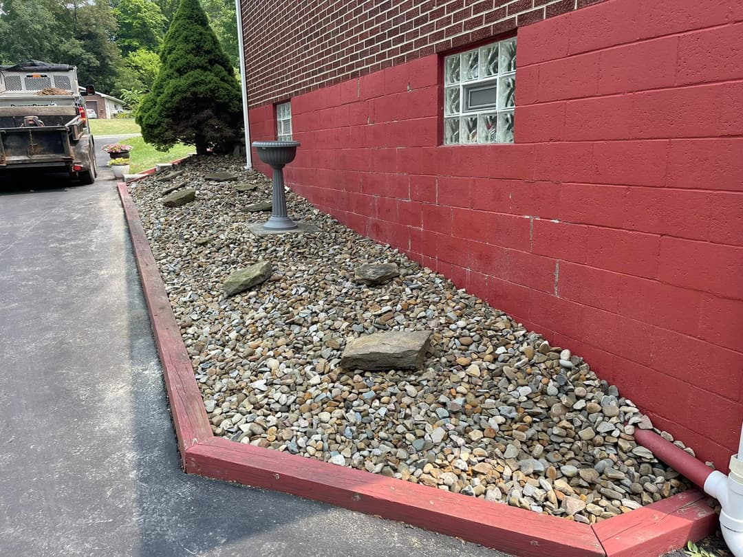Rock garden with decorative stones and red brick wall beside a paved driveway.