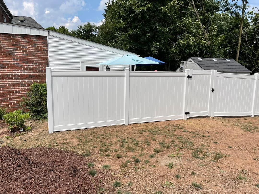 White vinyl fence enclosing a backyard with an umbrella and storage shed under a blue sky.