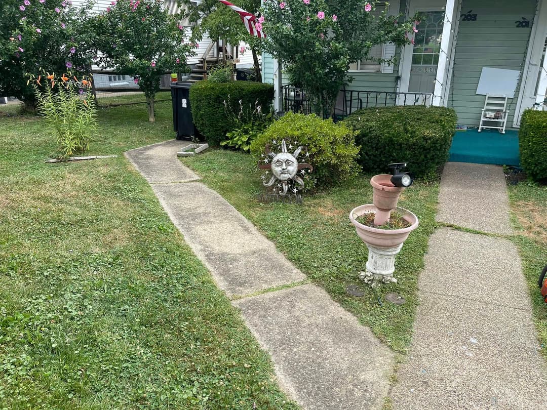 Pathway leading to a house with a sun sculpture and flower garden in the front yard.