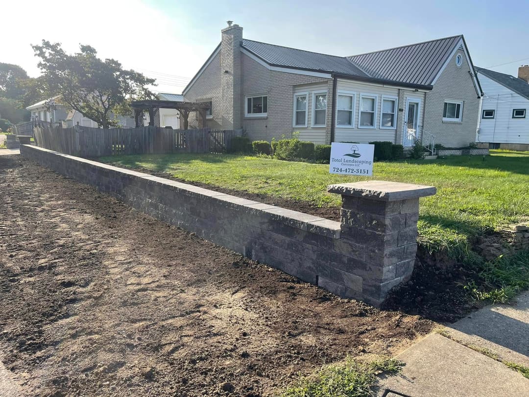 Residential landscaping with a stone wall, green lawn, and a house in the background.