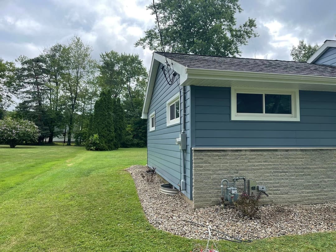Blue house exterior with landscaping and trees in the background on a cloudy day.