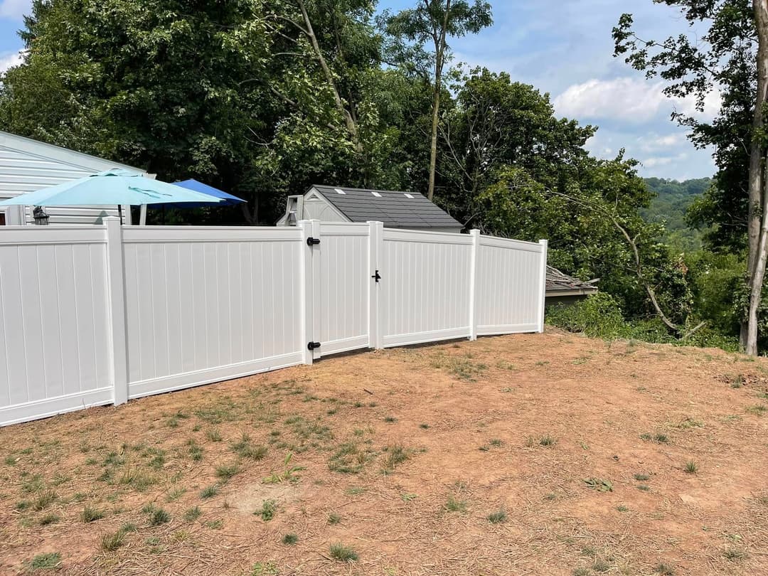 White vinyl fence in a backyard with a hillside view and a blue umbrella.