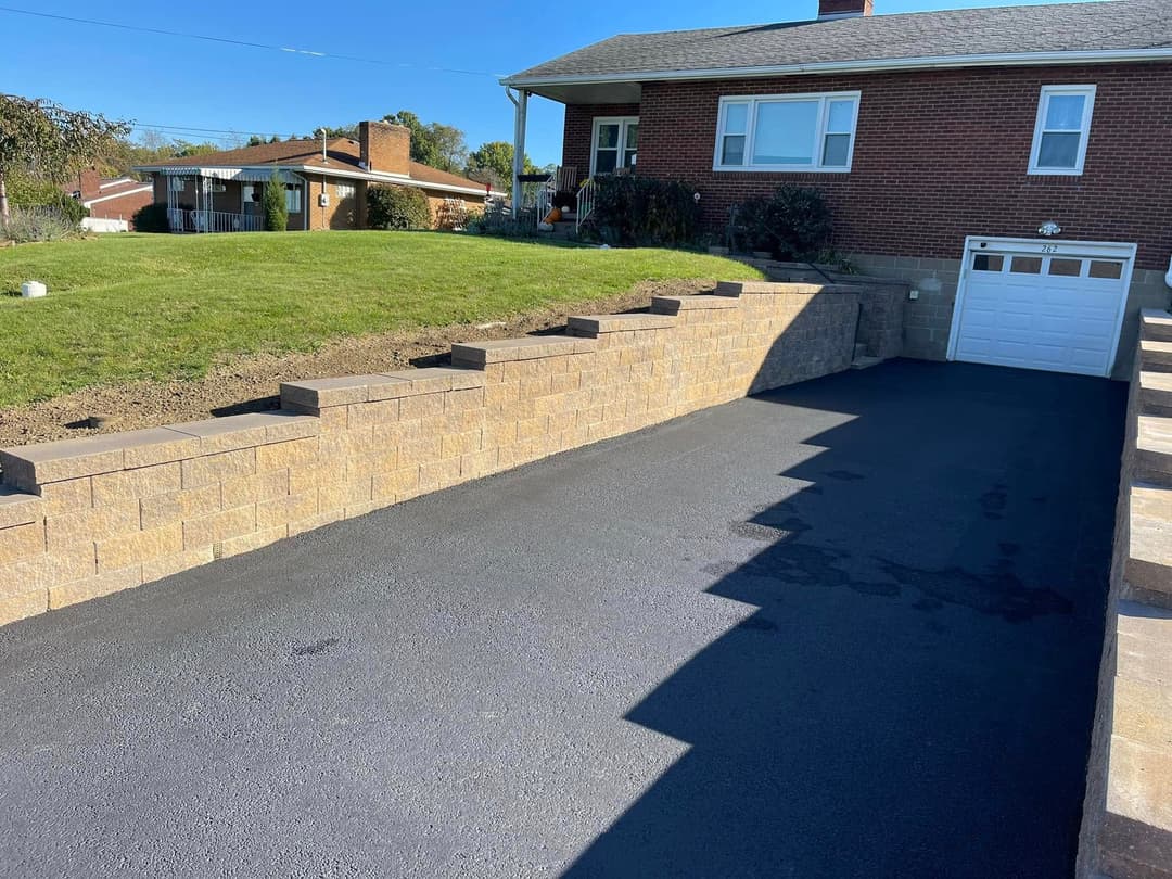 Newly paved driveway with stone retaining wall and suburban home background.