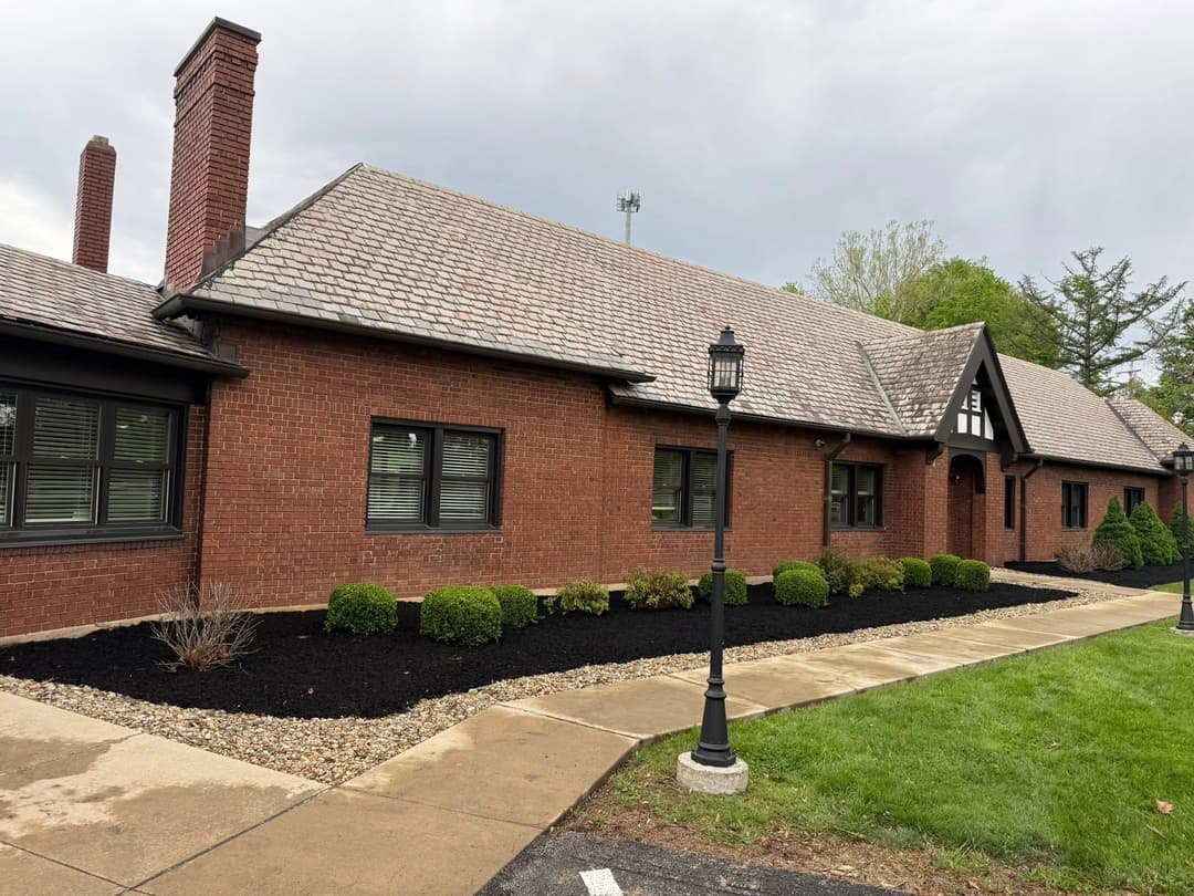 Brick building with a sloped roof, landscaped gardens, and black mulch pathway.