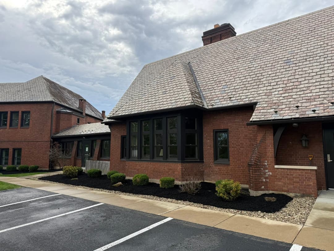 Brick building with a sloped roof and landscaped area, featuring parking spaces nearby.