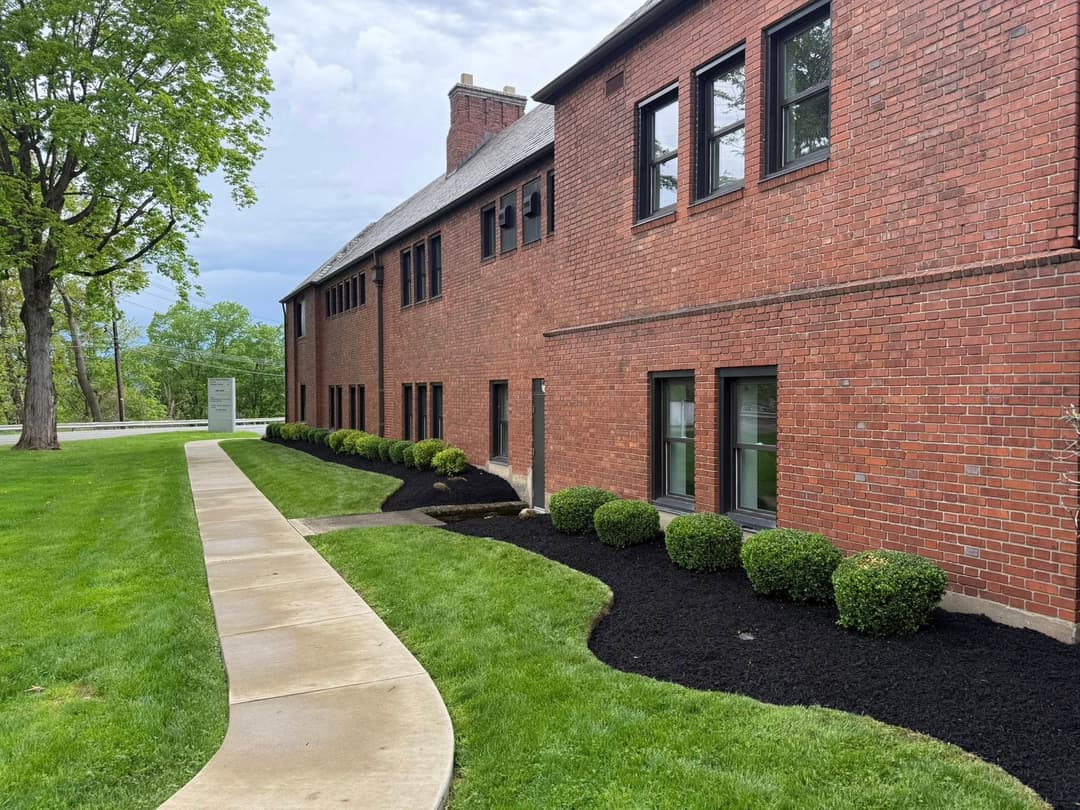 Red brick building with landscaped lawn and pathway, surrounded by trimmed bushes.