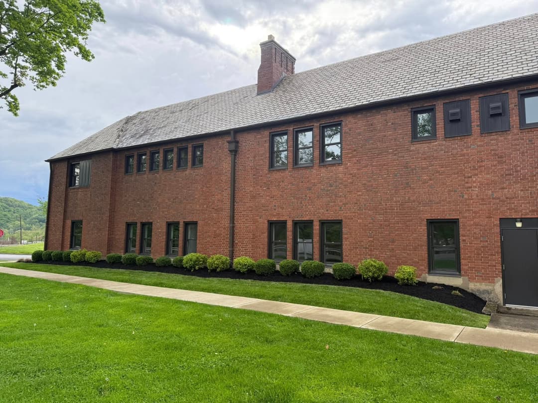 Brick building with multiple windows and landscaped lawn under a cloudy sky.