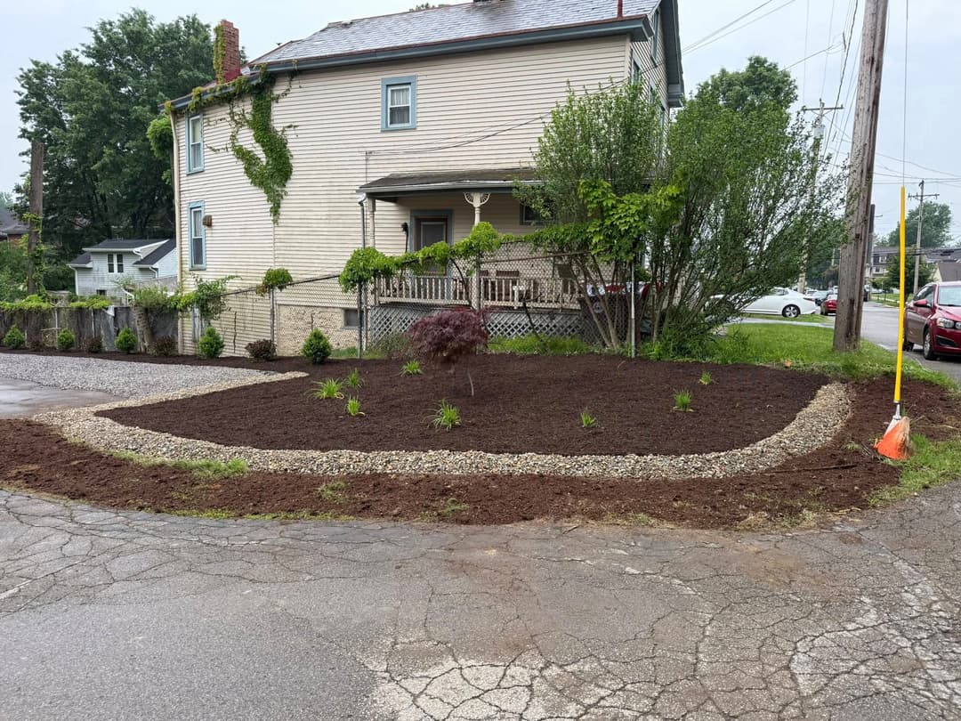 Landscaped front yard with mulch, plants, and gravel border surrounding a house.