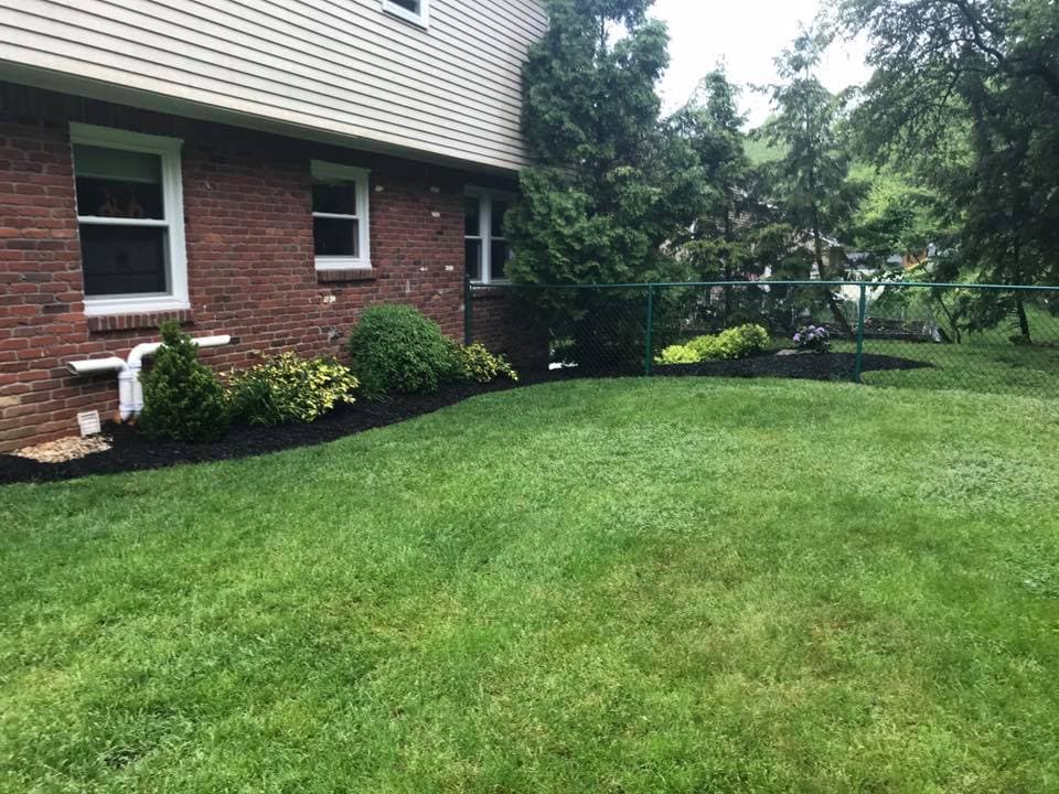 Lush green lawn with landscaped garden and fence surrounding a brick house.