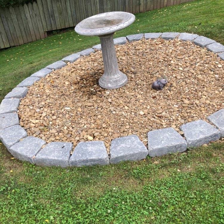 Birdbath surrounded by pebbles and stone edge in a landscaped garden.