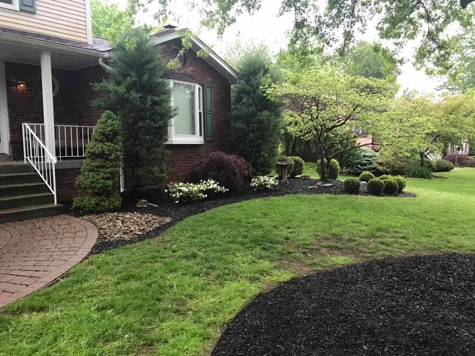 Beautiful landscaped front yard with shrubbery, trees, and stone pathway near a brick house.