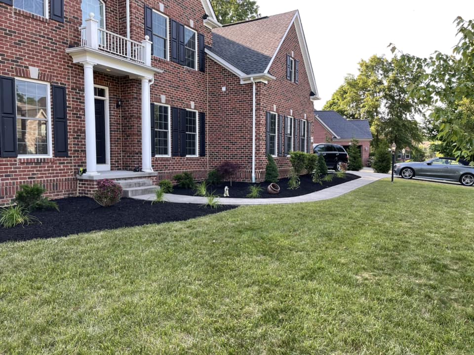 Brick house with manicured lawn, black mulch landscaping, and parked cars in the driveway.