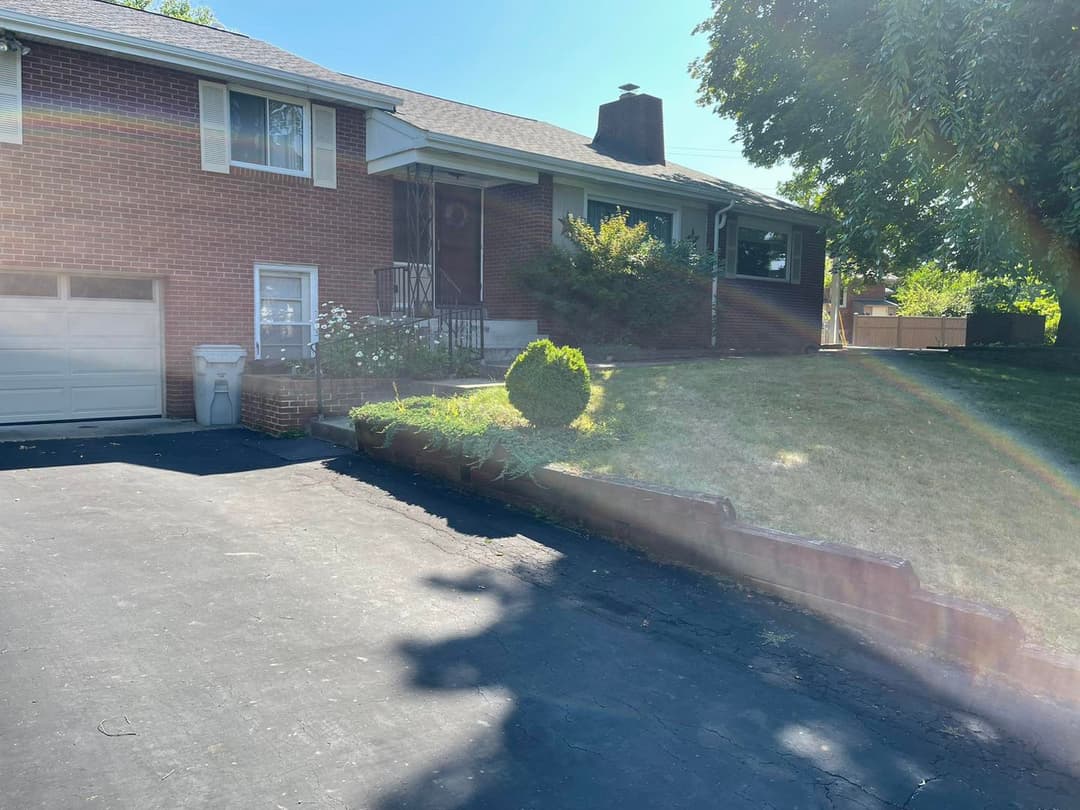 Brick house exterior with driveway, landscaped front yard, and sunny outdoor setting.