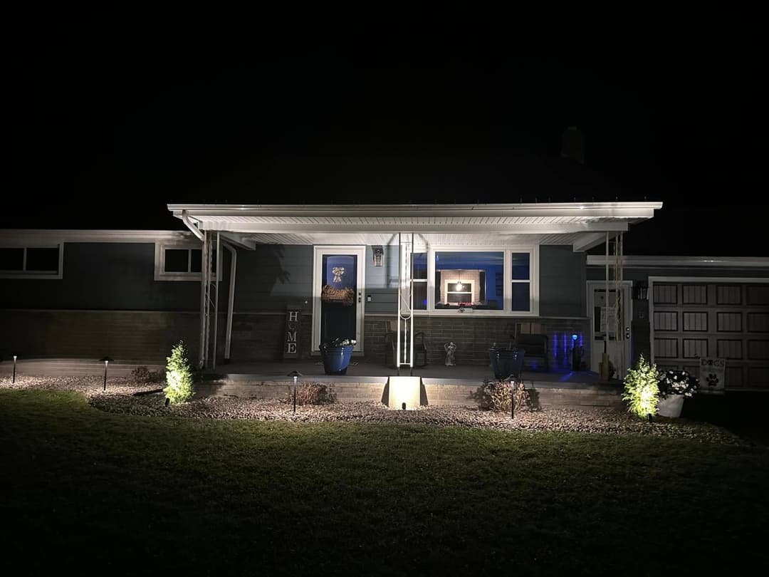 Front view of a well-lit modern home at night, featuring landscaped yard and stylish porch.
