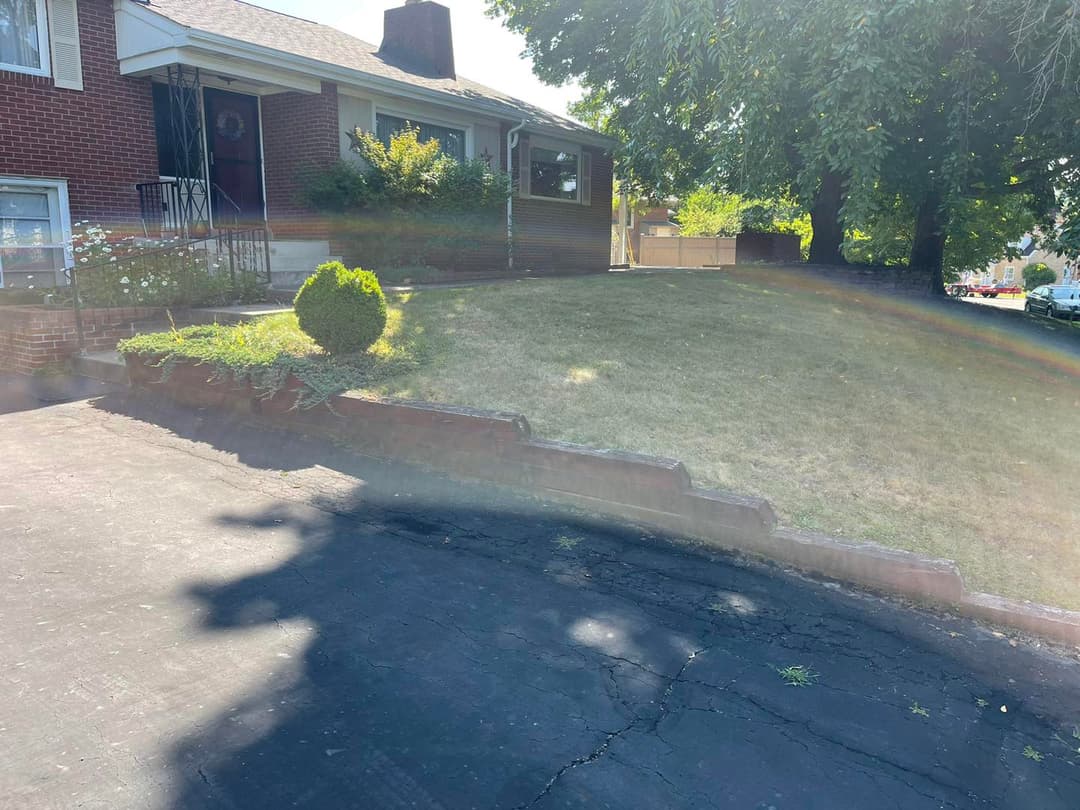 Front yard of a brick house featuring a landscaped garden and driveway on a sunny day.