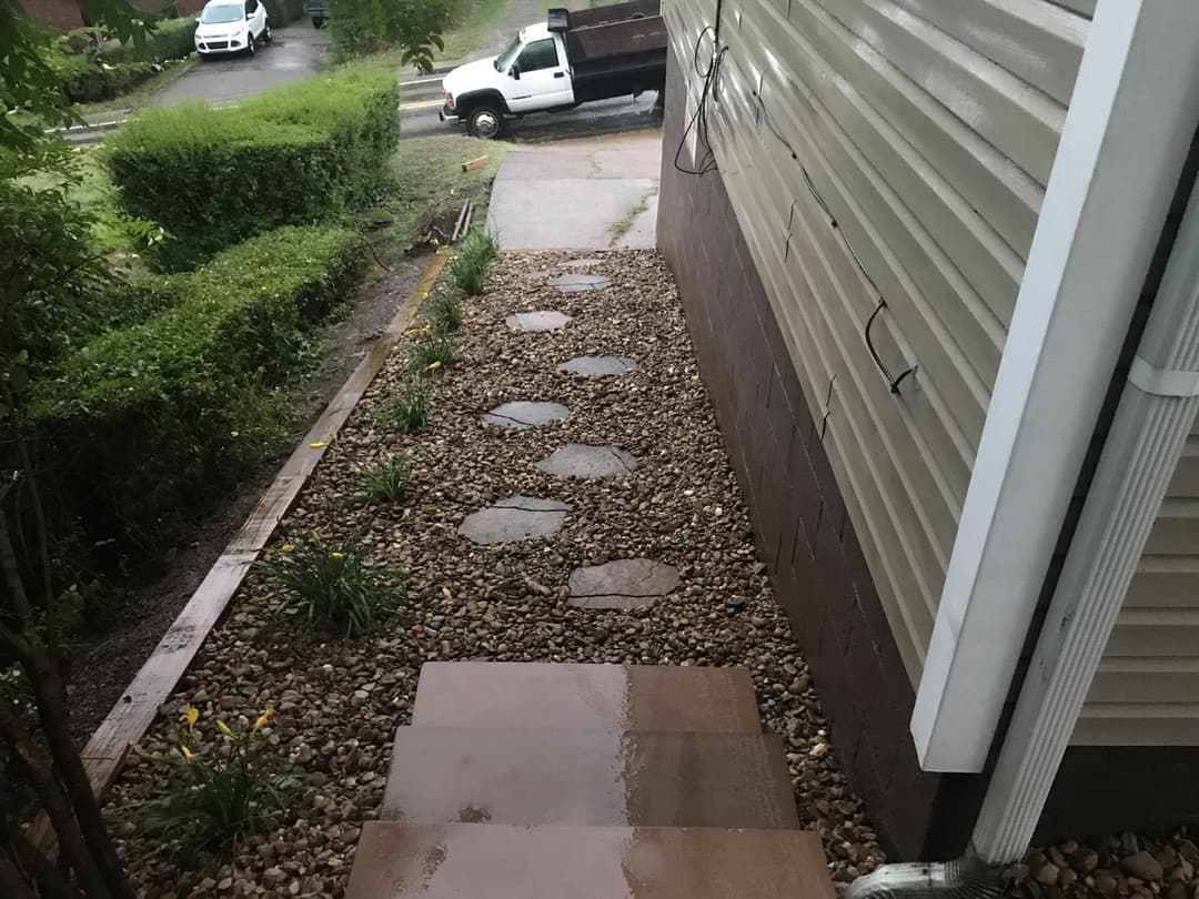 Pathway lined with stones and plants leading to a house, with rain-soaked steps visible.
