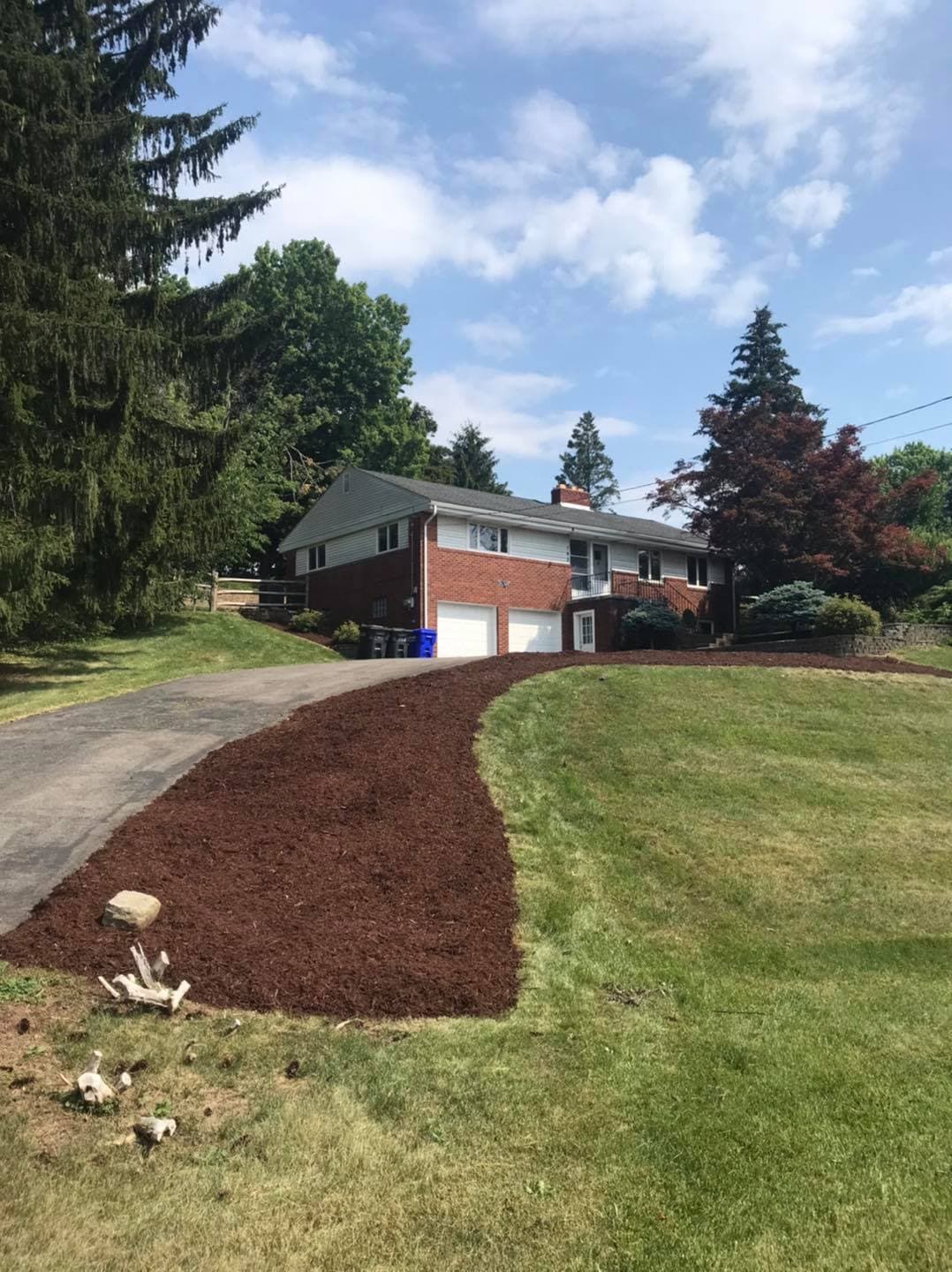 Brick house with newly mulched garden and a sloped driveway, surrounded by trees.