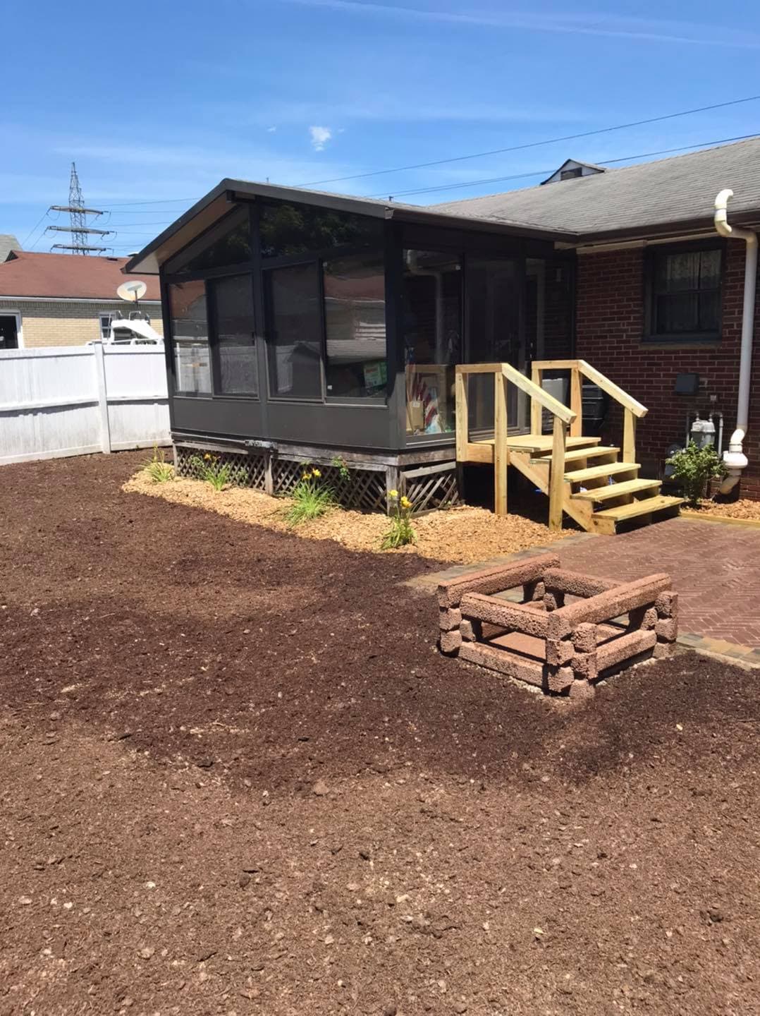 Sunroom addition with wooden steps, surrounded by freshly mulched garden area and patio bricks.