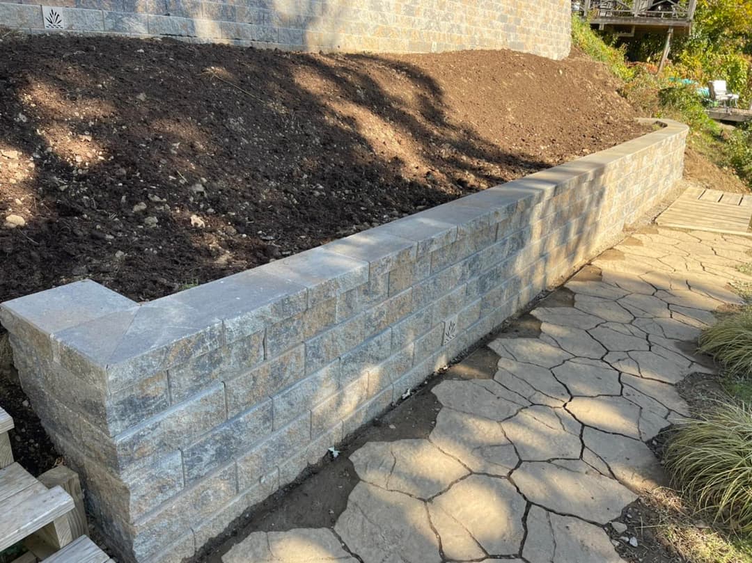 Stone retaining wall next to a dirt hill and a stone pathway in a garden landscape.