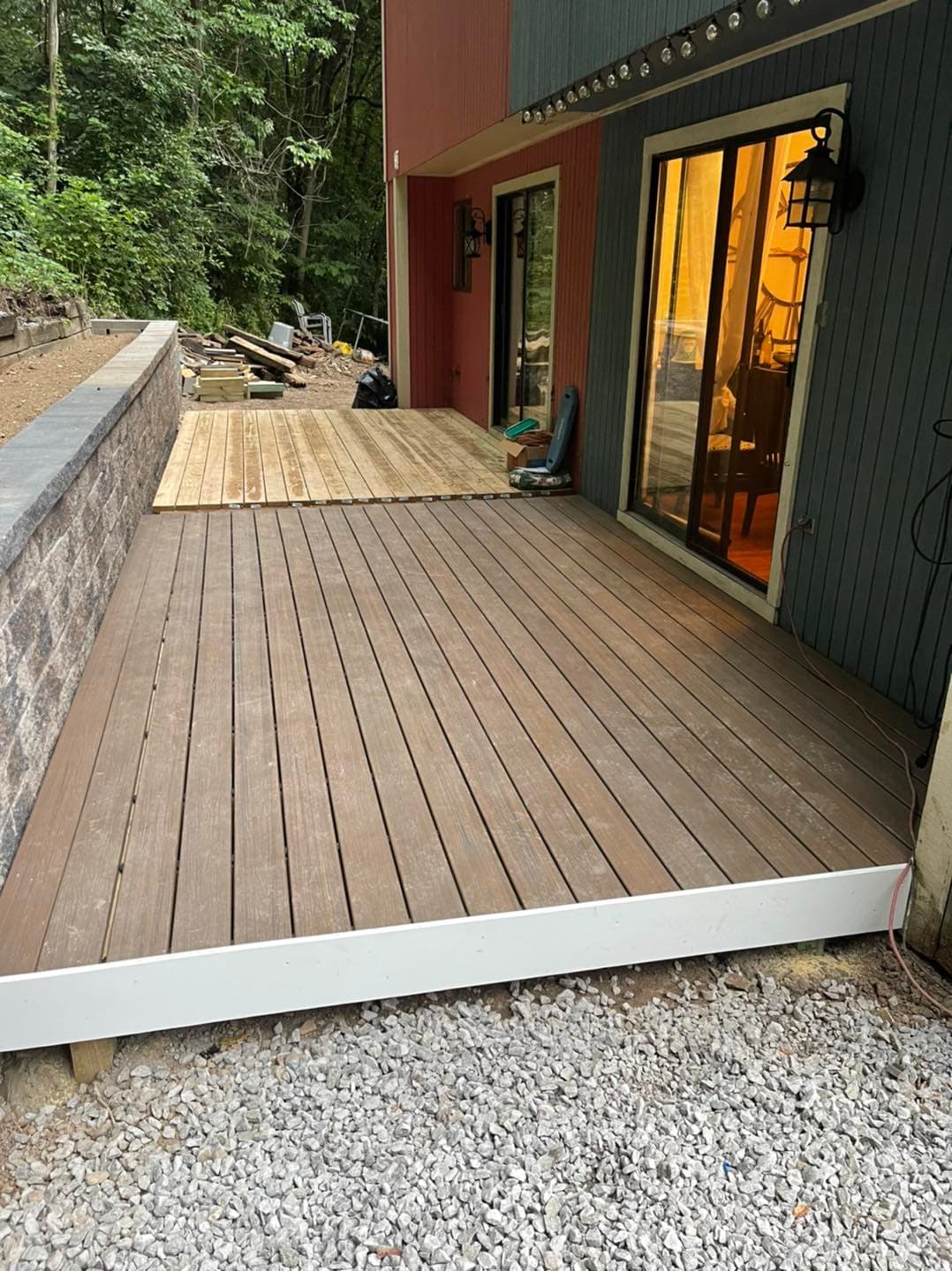 Newly constructed wooden deck next to a modern house with glass doors and outdoor lighting.