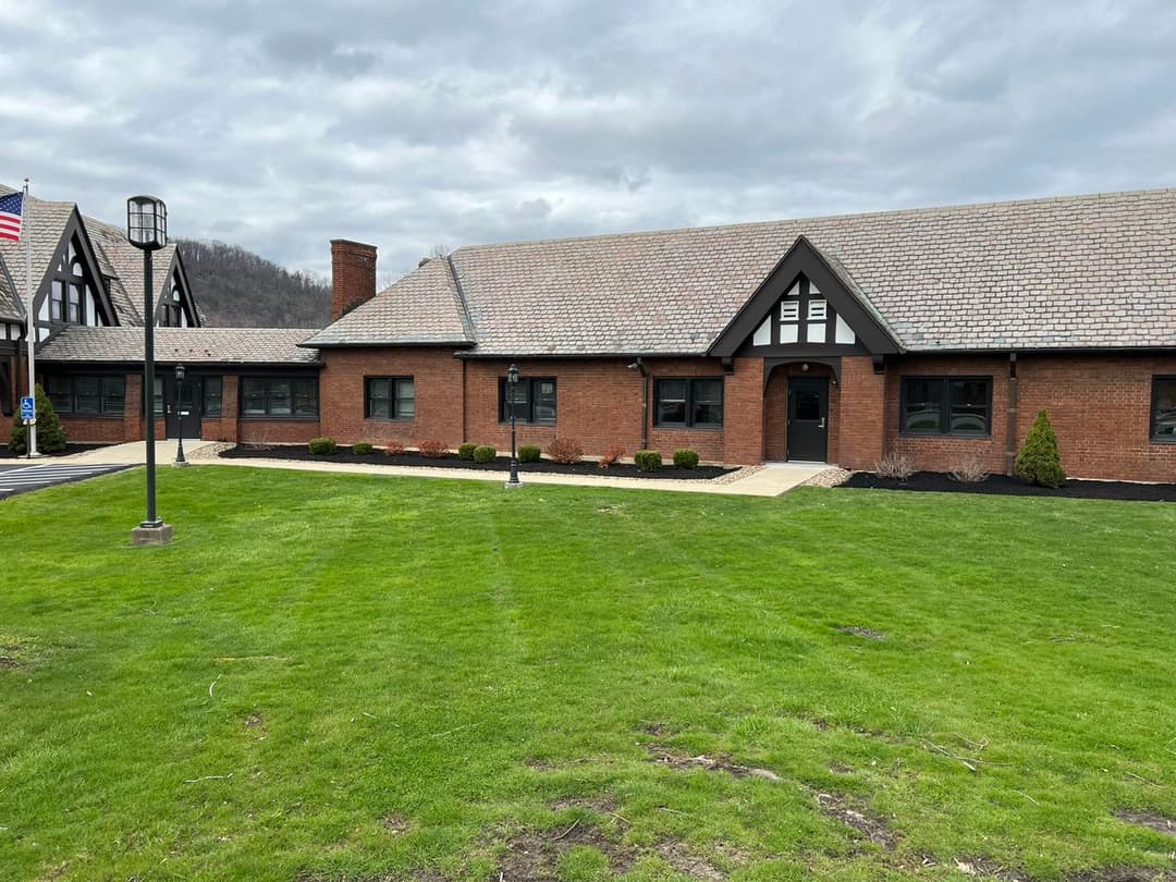 Historic brick building with Tudor-style architecture set on a grassy lawn under a cloudy sky.