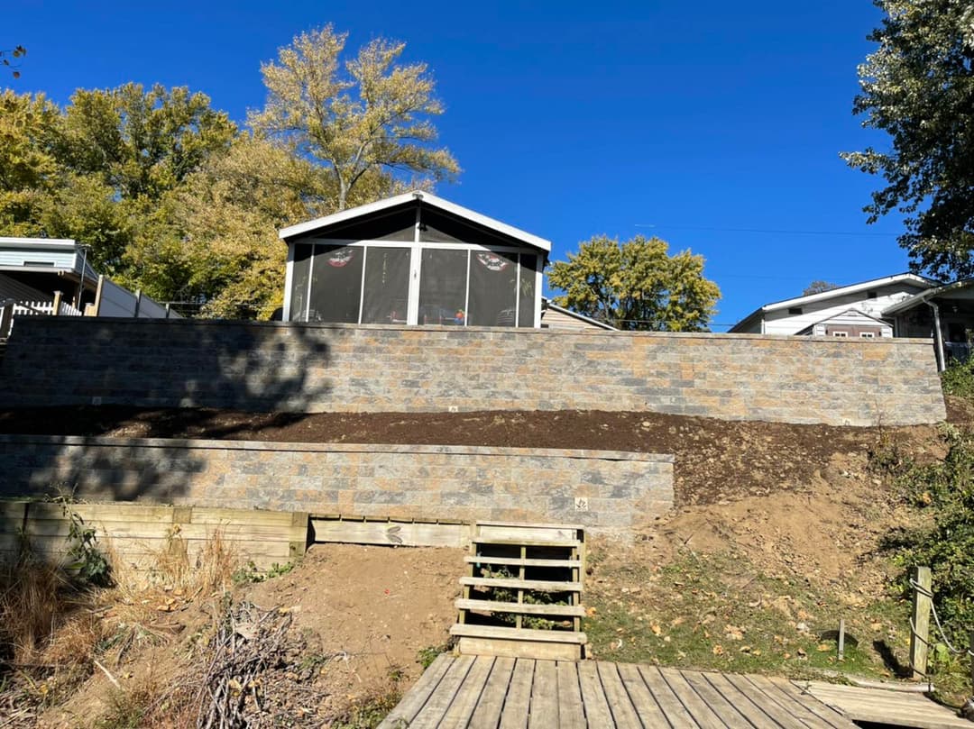 Exterior view of a house with a stone retaining wall and wooden steps, under a clear blue sky.