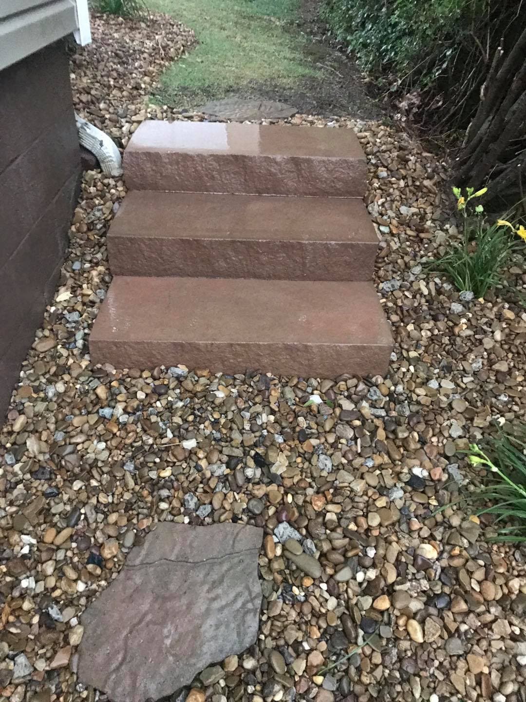 Stone steps leading to a grassy area, surrounded by pebbles and yellow flowers.
