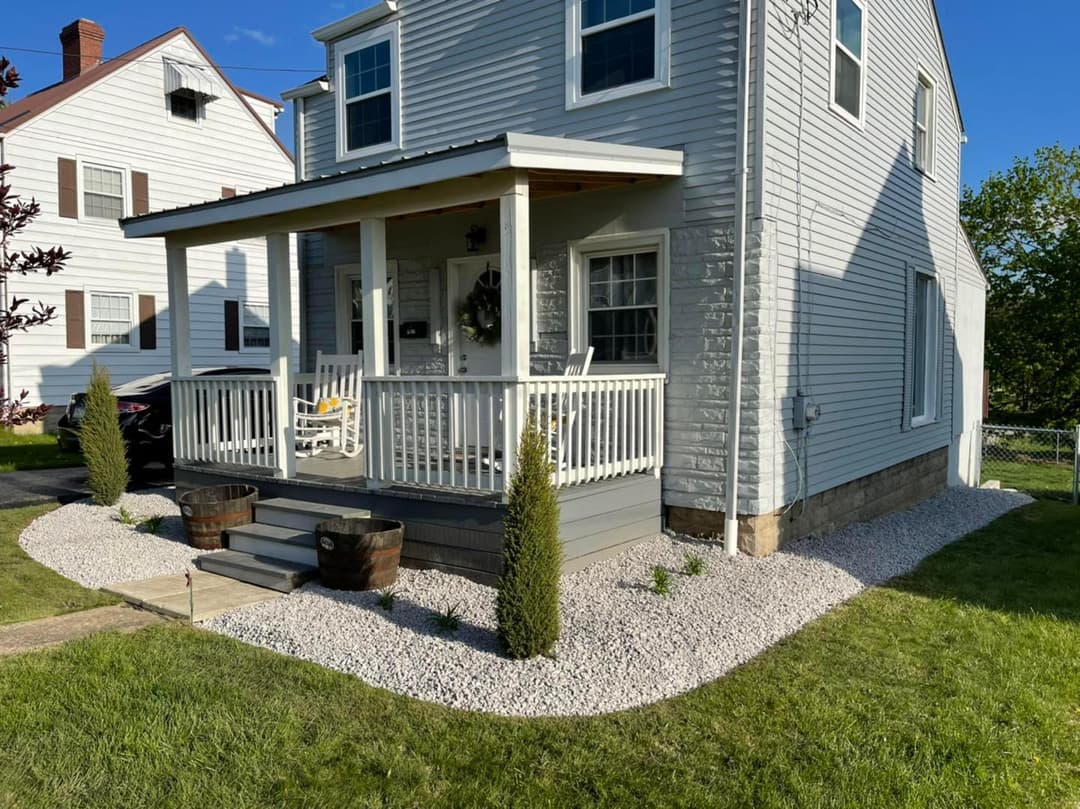 Cozy home with a front porch, decorative stones, and small shrubs in the yard.