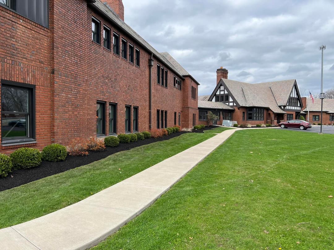 Red brick building with landscaped lawn and pathway, cloudy sky overhead.