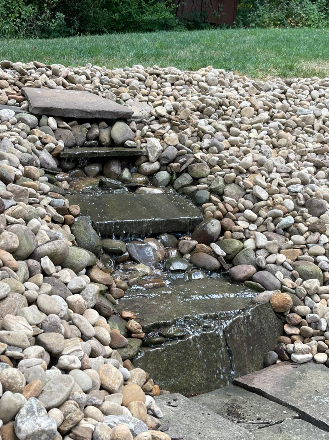 Water trickles down a stone pathway surrounded by smooth pebbles in a serene garden setting.