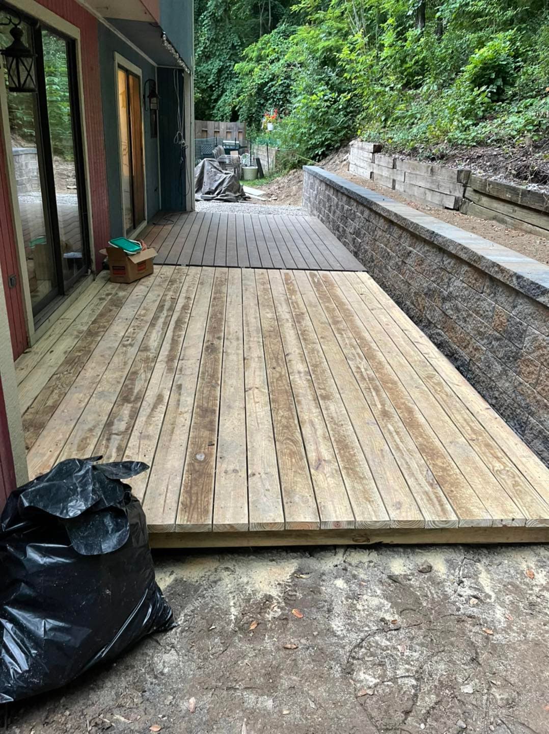 Newly constructed wooden deck alongside a landscaped stone wall in a wooded area.