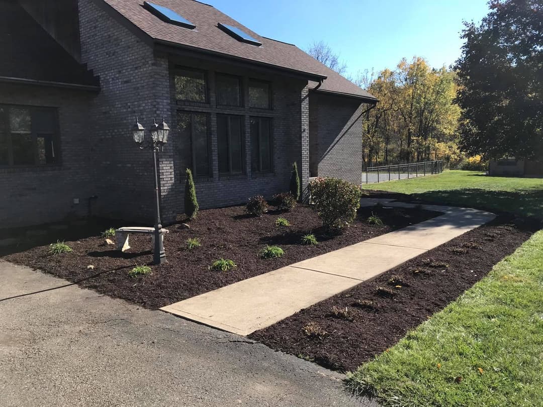 Landscaped front yard with mulch, plants, and a pathway beside a brick house.