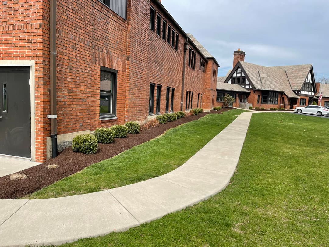 Brick building exterior with landscaped path and manicured shrubs on a sunny day.