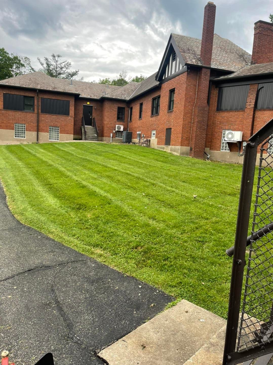 Lawn maintenance at a brick building with air conditioning units and a cloudy sky backdrop.
