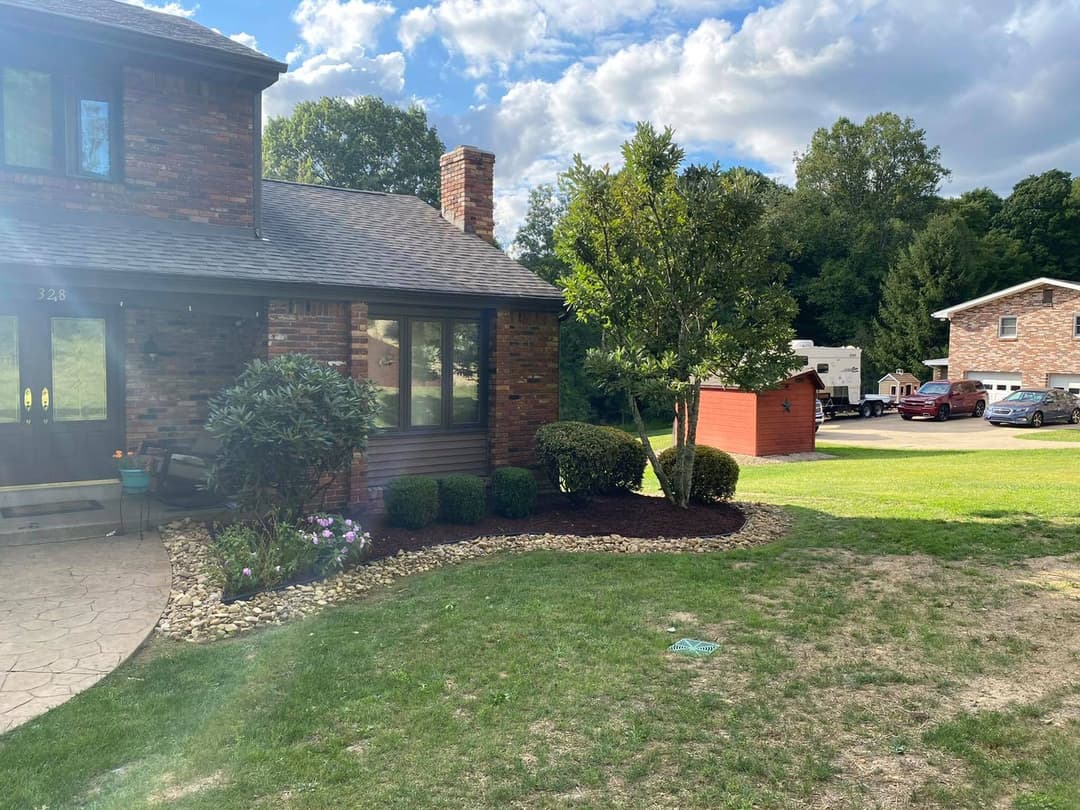 Brick house with lush landscaping, garden beds, and a clear blue sky in the background.