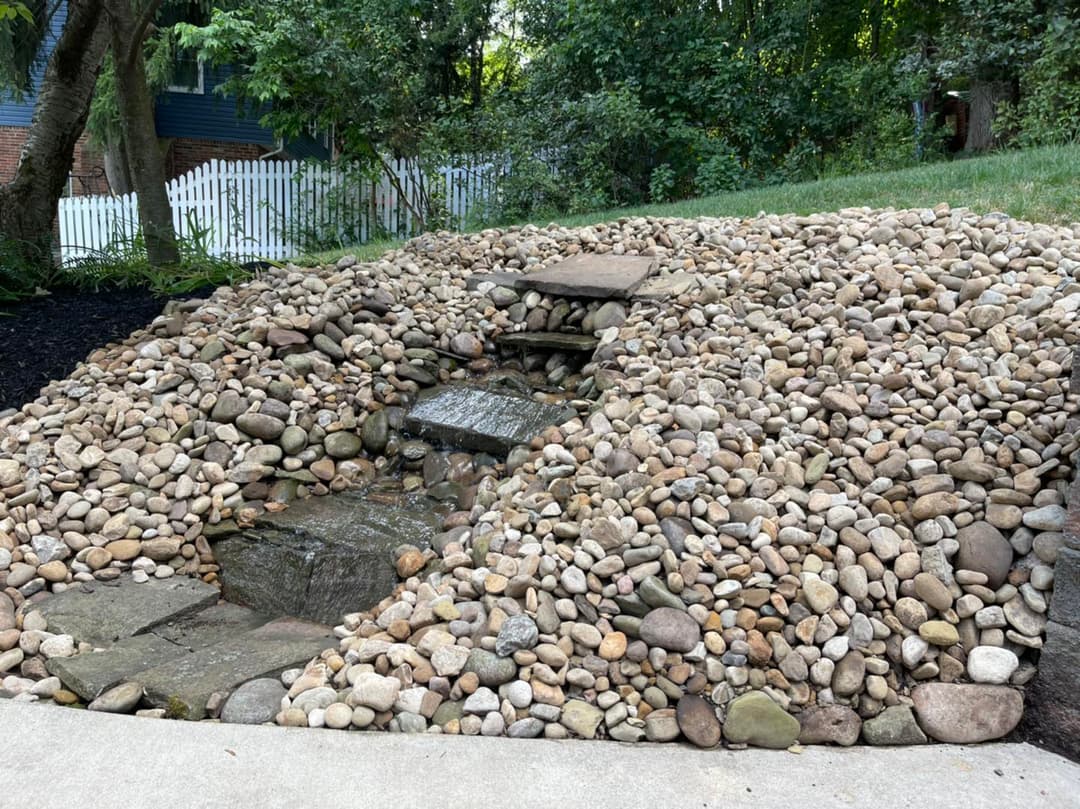 Landscape featuring a rock garden with stone steps and a small water feature surrounded by greenery.