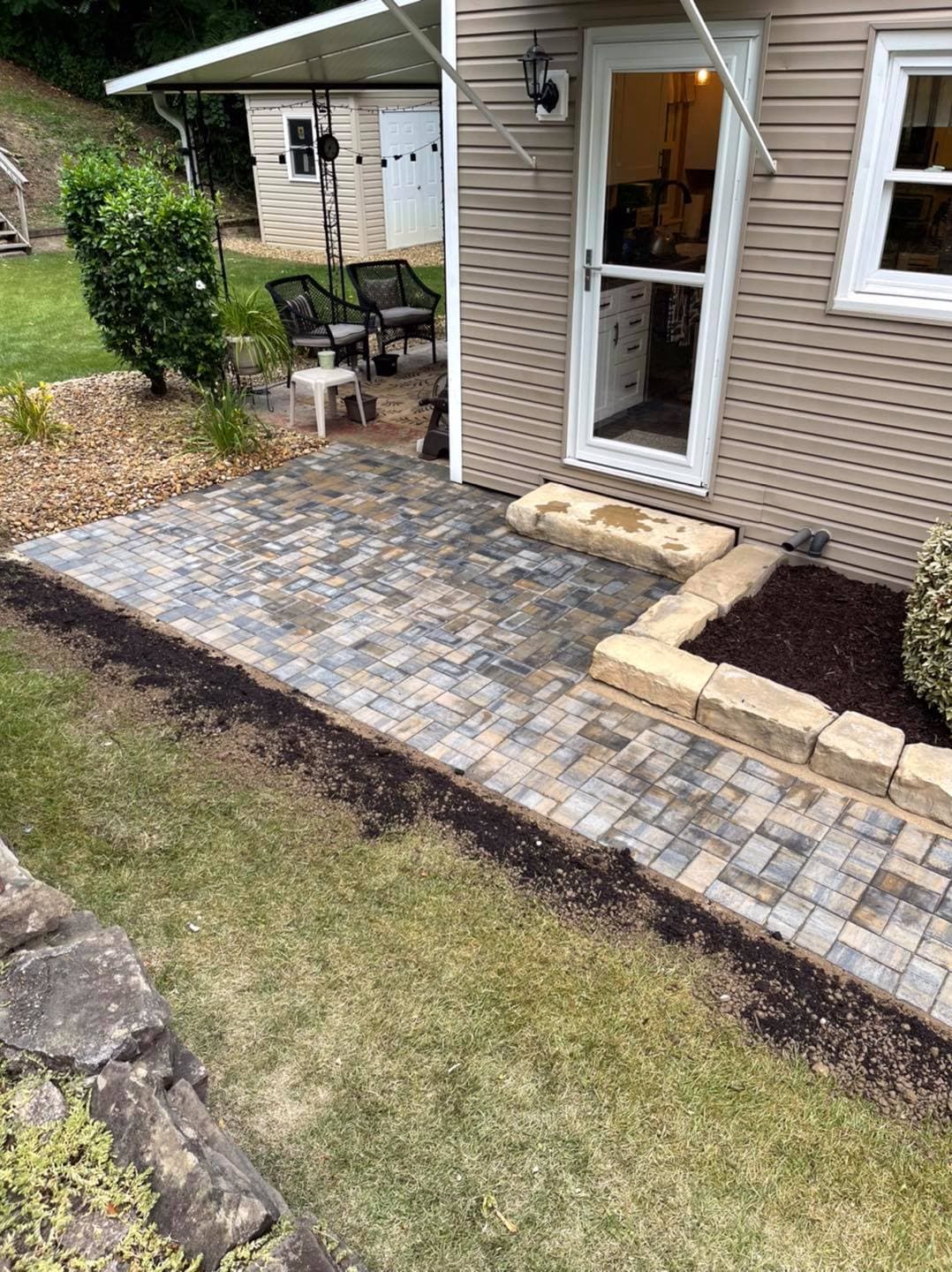 Paver patio installation beside a house with landscaping features and a seating area.