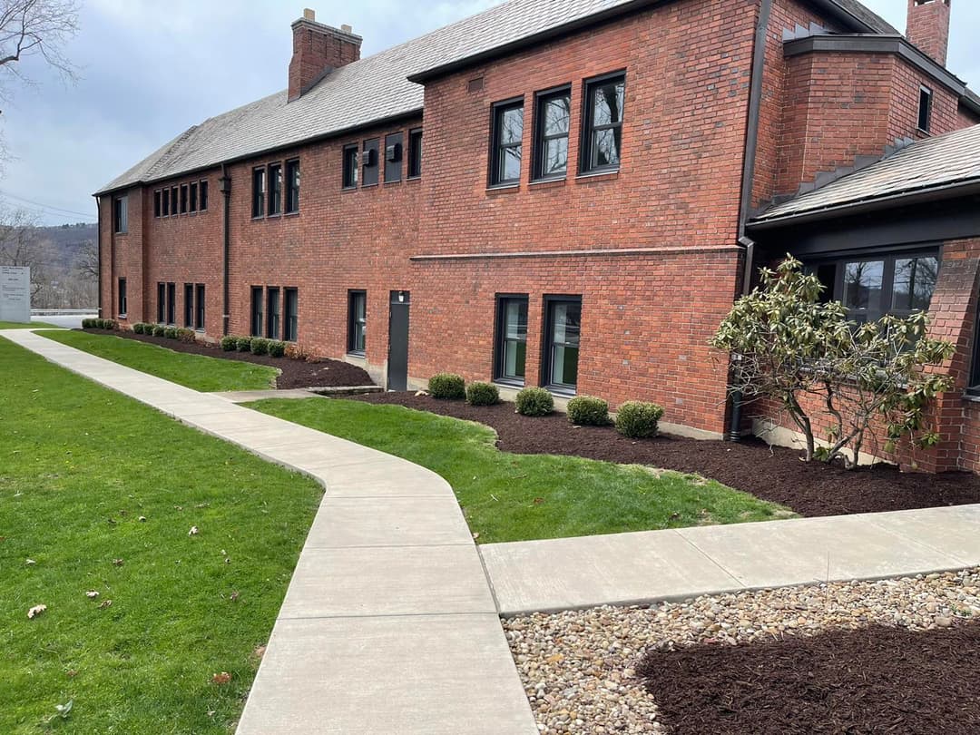 Brick building exterior with landscaped pathway, shrubs, and mulch in a serene setting.