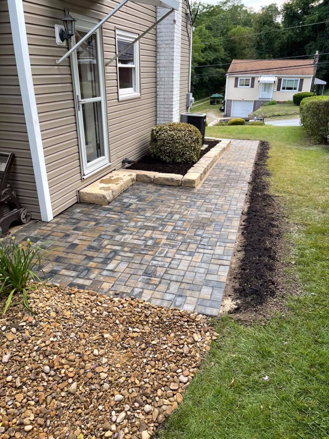 Newly paved patio with stone borders, grassy area, and a landscaped garden near a residential home.