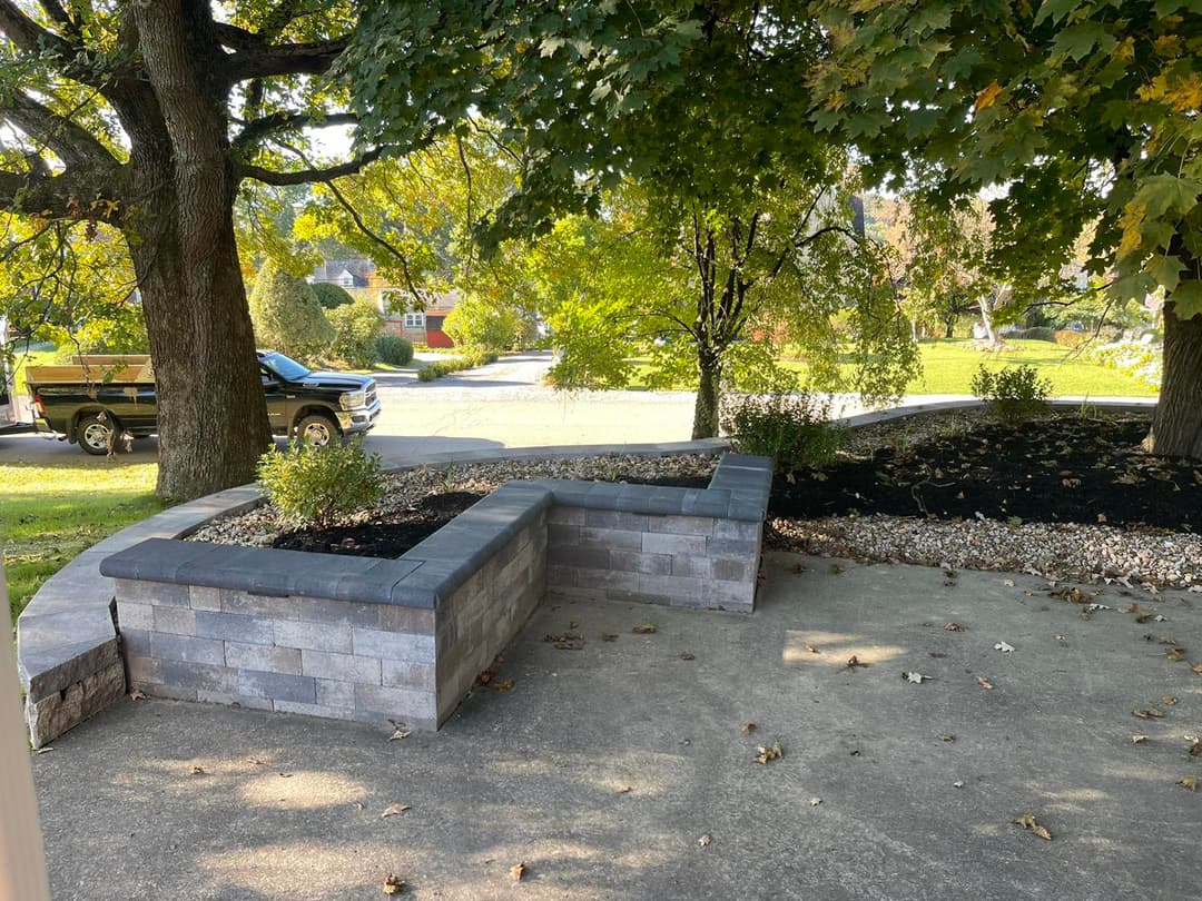 Stone retaining wall with landscaping in a residential garden and tree shaded area.
