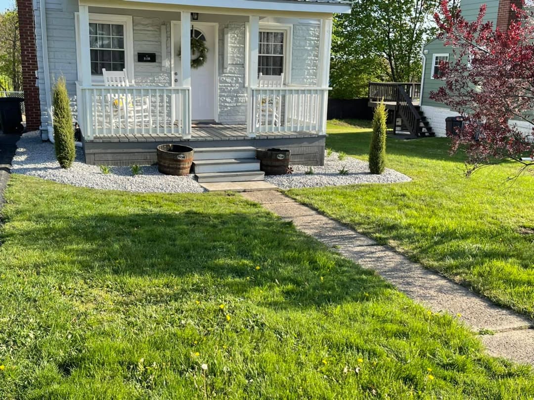 Charming front porch of a house with landscaped garden and pathway, featuring decorative plants.