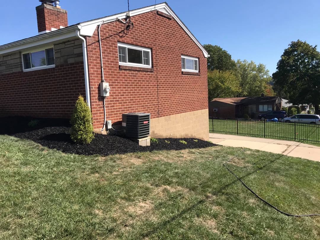 Brick house exterior with air conditioning unit, green lawn, and nearby trees on a sunny day.